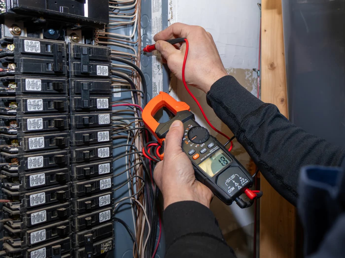 Electrician testing circuit breakers in an electrical panel with a clamp meter